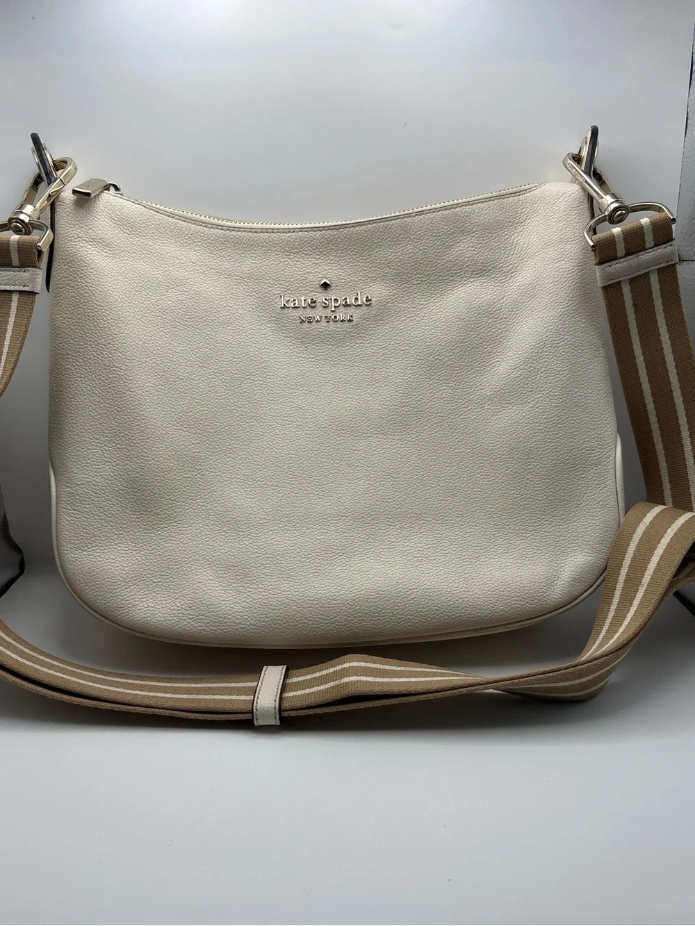 Kate Spade New York cream leather crossbody bag featuring a striped webbing Stra